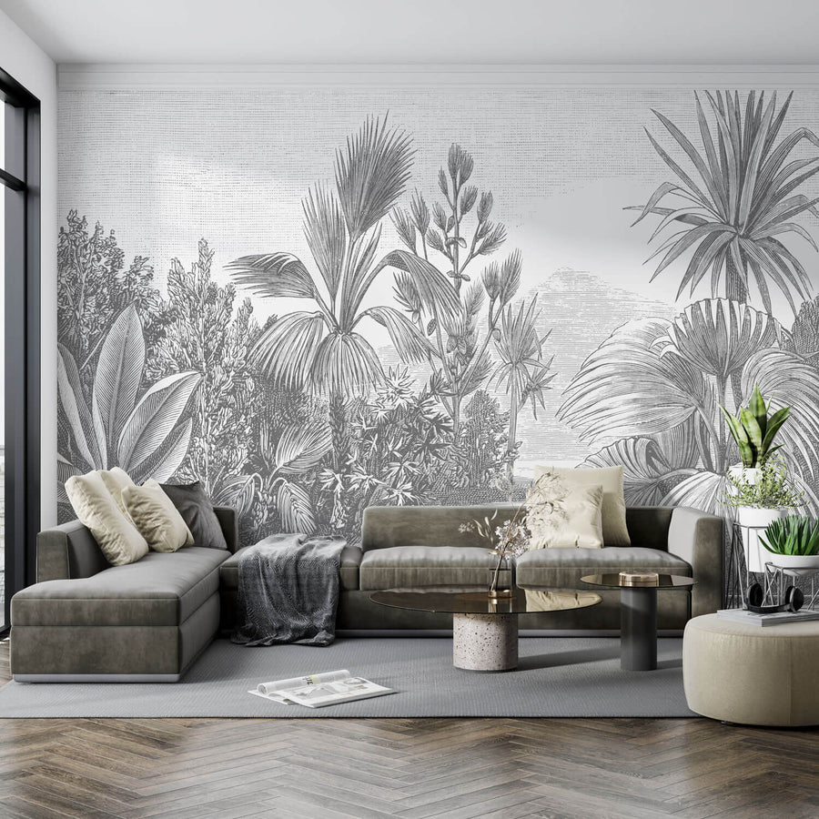 Edles Wohnzimmer Interieur mit einer hellgrauen Fototapete mit Palmen und Büschen. Davor steht eine dunkelgrüne Couch mit Deko in beige.